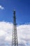 Cell tower against blue sky with clouds. A cell site or tower with antennae and telecommunications equipment is part of cellular