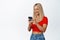 Cellular technology. Young blond woman using mobile phone and smiling, messaging or placing an oder on smartphone, white