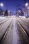 Center of the snowy road with rails. The night city with night traffic.