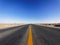 Centered view of an endless asphalt road in desert, low angle straight rough road with blue sky background, magic world