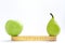 A centimeter, an apple and a green pear stand on a white background