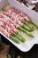 ceramic baking dish with aspargus covered with bacon on wooden kitchen table