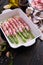 ceramic baking dish with aspargus covered with bacon on wooden kitchen table