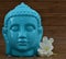 Ceramic Blue color Serene face statue of Buddha with flowers on wooden backdrop