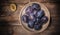 Ceramic bowl with plums over dark wooden board and a half of plum near it. Fruit background. Top view.