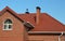 A ceramic, clay roof of a brick house with a chimney, flashing, attic window, a weather vane, fascia, and soffit, and a roof