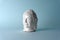 Ceramic head of a Buddha on a blue background. Minimal concept, copy space