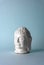 Ceramic head of a Buddha on a blue background. Minimal concept, copy space
