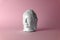 Ceramic head of a Buddha on a pink background. Minimal concept, copy space