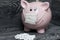 Ceramic piggy bank in pink. With a gauze bandage. In front of her is a handful of white pills. Treatment savings during an