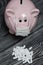 Ceramic piggy bank in pink. With a gauze bandage. In front of her is a handful of white pills. Treatment savings during an