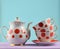 Ceramic teapot, a stack of cups in polka dots on a wooden table isolated on a blue pastel background. Copy space.