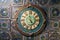Ceramic wall clock with roman dial against the background of ancient fireplace tiles