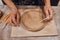 A ceramist in a pottery workshop makes patterns on a clay plate using tools.