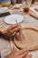 A ceramist in a pottery workshop makes patterns on a clay plate using tools.