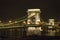 Chain Bridge of Budapest is lit at night with view of Danube River.