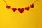 A chain of five red hearts carved from the fleece on the top edge on a yellow background with a copy space