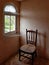 A chair next to a corner window with webs