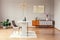 Chair at table under gold lamp in living room interior with poster above cupboard with plant. Real photo