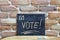 Chalk board with the word VOTE! drown by hand and chalks on wooden table on brick wall background