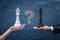 A chalk question mark between a female hand with a white chess king and a male hand with a black king.