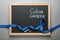 Chalkboard with blue awareness ribbon and words COLON CANCER on grey background, top view