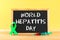 Chalkboard with text World Hepatitis Day. June 28th. A green jade ribbon and a syringe with blood on a wooden table against the ba