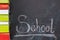 On the chalkboard written the word school and on the left vertically lie in a row of books