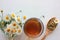 Chamomile herbal tea in a glass cup, dried medical flowers in the wooden spoon, and bouquet of white daisies in a glass vase