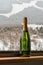 Champagne bottle on windowsill through the glass in the raindrops over mounains background