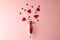 Champagne glass spilling red heart shapes and confetti on pale pink background with copy space