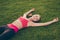 Champion. Well done! Exhausted cheerful sportive woman is relaxing after a fitness workout, lying on the green grass in a spring