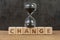 Change, transform or evolve concept, sand glass or hourglass on cube block with alphabet building the word Change on wood table