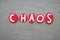 Chaos word composed with red colored stone letters over green sand