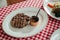 Charcoal grilled wagyu Ribeye steak served with BBQ sauce and baked potato in white plate on red and white pattern tablecloth