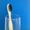 Charcoal infused bamboo toothbrush in glass on navy blue background. square.