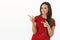 Charismatic friendly brunette woman in red t-shirt sassy pointing finger pistols left at blank white copy space, smiling