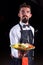 Charismatic waiter carries cooked dish on a black background.