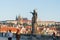 Charles Bridge before sunrise tourists walking across under staute of St John Baptist pointing way.