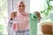 Charming Arab Muslim woman in hijab smiles toothy smile looking at camera, holding a rag and detergent spray for washing windows