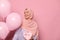 Charming Arab Muslim woman in pink hijab and blue pastek shirt, posing with bunch of helium balloons on pink background