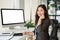 A charming Asian female call centre operator with a headset sits at her desk in the office