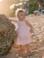 Charming baby in pink dress on sandy beach with sunset tones