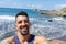 Charming bearded latino sharing selfie in social media in the beach with close eyes because of the sun. Tan Fit muscle surfer with