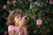 Charming blond child on background of flowers in summer. Pretty little child working in garden, child taking care of