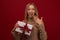 Charming blonde woman holding gift with red ribbon. Studio shot red background. New Year Birthday Holiday concept