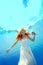 A charming bride with red hair swims and poses for the camera underwater in the pool in a white dress with flowers in her hand on