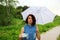 Charming brunette in denim dress with a cup of coffee under a white umbrella in nature. sprinkle