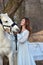 Charming brunette in pale blue dress with a white horse