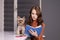 Charming brunette woman in brown golf with blue notebook and a Yorkshire Terrier puppy sitting at table in gray room. pet, animal